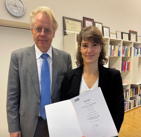 Two people standing in an office, one holding a certificate from KIT.